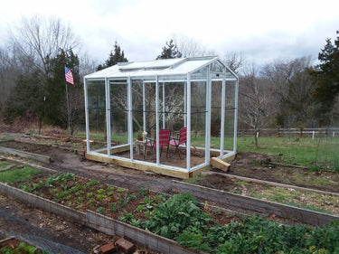 White Janco greenhouse 8x10 with transparent panels, showcasing a sturdy frame and spacious interior for plant cultivation.